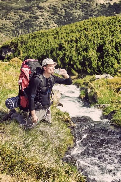 Turysta, relaks w pobliżu górskiej rzeki i picia wody butelkowanej — Zdjęcie stockowe