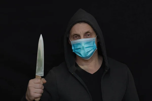 头罩里藏着一个男人 戴着医疗面罩 拿着一把刀 看着被黑色背景隔离的相机 Covid 19大流行病期间的抢劫 暴力和经济危机概念 黑白摄影 — 图库照片