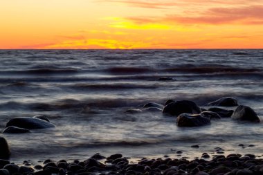 Uzun süre deniz ve kayalara maruz kalmış. Dalgalı denizden çıkan kayalar. Renkli gün batımı.