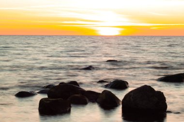 Uzun süre deniz ve kayalara maruz kalmış. Dalgalı denizden çıkan kayalar. Renkli gün batımı