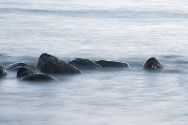 Long exposure of sea and rocks. Boulders sticking out from smooth wavy sea. Tranquil scene.