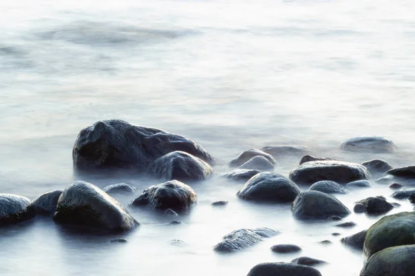 Long exposure of sea and rocks. Boulders sticking out from smooth wavy sea. Tranquil scene.