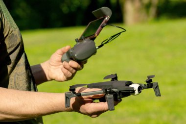 Uzaktan kumandalı cep telefonu olan adam İHA 'yı bekletiyor. Güneşli yeşil doğa arka planı.