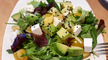 Avokado, mozzarella, roka ve beyaz restoran tabağında sarı kiraz domatesli yeşil salata. Sağlıklı organik vejetaryen salatası..