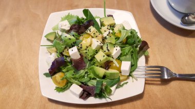 Avokado, mozzarella, roka ve beyaz restoran tabağında sarı kiraz domatesli yeşil salata. Sağlıklı organik vejetaryen salatası..