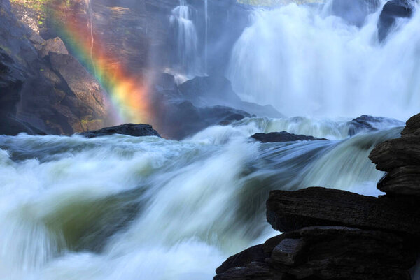 Радуга появляется в тумане бушующей реки. Символ чудес, красоты в природе и божественных сокровищ.