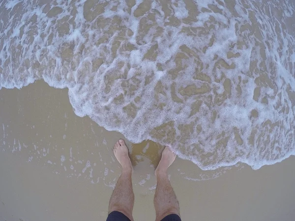 Jambes masculines sur la plage de sable avec de l'eau mousseuse — Photo