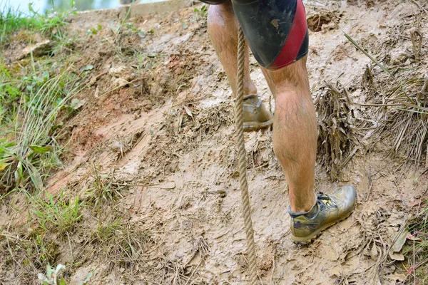 Неузнаваемый человек в грязи, взбирающийся по веревке — стоковое фото