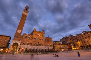 Siena, İtalya - 3 Temmuz 2018: Mangia Kulesi ile Campo Meydanı Siena, İtalya 'nın dönüm noktası. Gün batımında meydanda oturan gençler