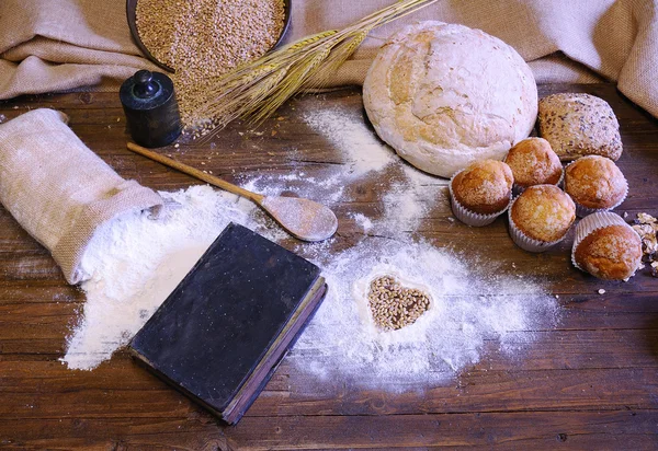 Different types of bread, fruit cakes and scattered flour on woo — Stock Photo, Image