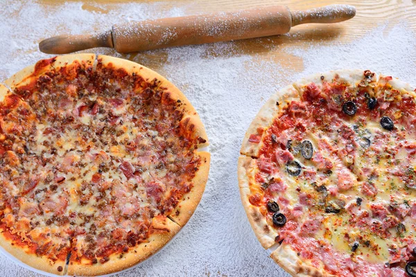 Dwa pyszne pizze na drewnianym stole rozrzucone z mąki — Zdjęcie stockowe