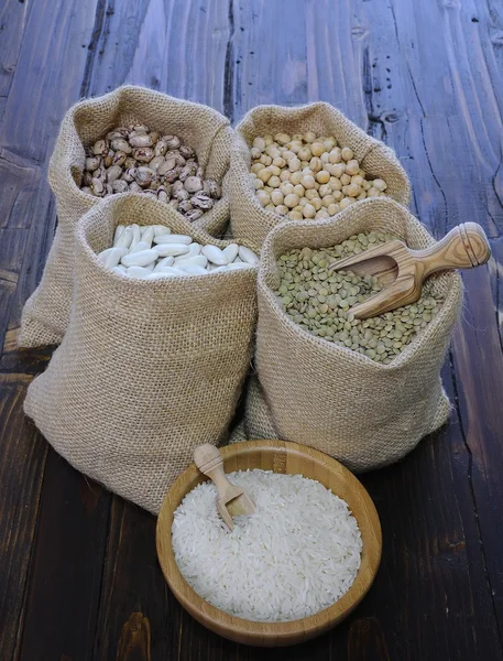 Diferentes tipos de ervilhas em sacos têxteis e arroz branco em tigela — Fotografia de Stock