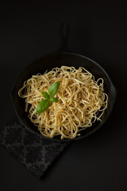 Fesleğenli siyah arka plan üzerine bir dökme demir tavada ince erişte