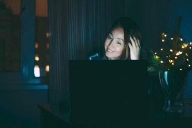 Çekici, gülümseyen, esmer, orta yaşlı bir kadın. Evde dizüstü bilgisayar kullanıyor, geceleri çalışıyor.