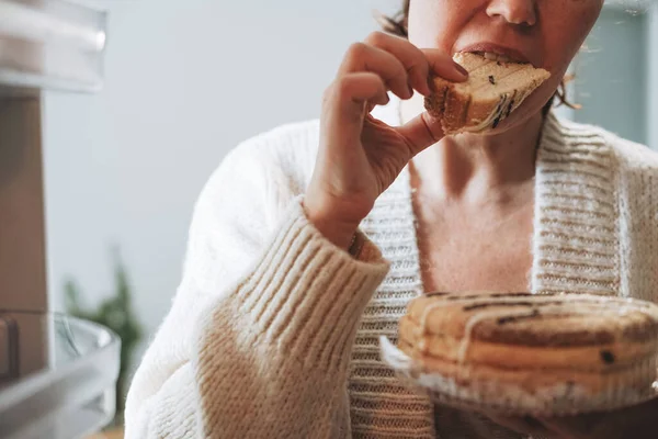 魅力的なフレンドリーなブルネット女性中年で居心地の良いカーディガン食べるケーキから冷蔵庫でキッチンに自宅 — ストック写真