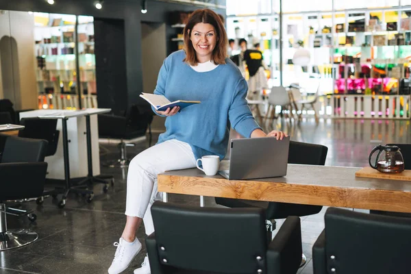 Beautiful stylish young woman plus size body positive using laptop at the beauty salon office, small business owner