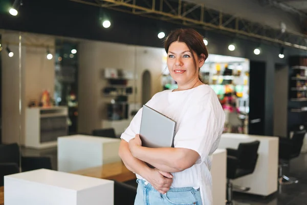 Beautiful stylish young woman plus size body positive with laptop at the beauty salon office, small business owner