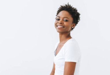 Beyaz arka planda izole edilmiş beyaz tişörtlü güzel, mutlu Afro-Amerikan kadın portresi.
