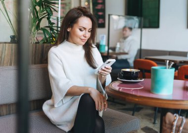 Çekici, esmer, beyaz günlük elbiseli, kahve fincanı olan, kafede cep telefonu kullanan bir kadın.
