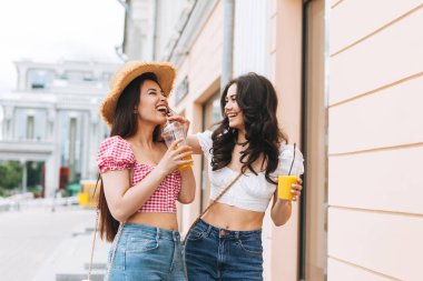 Mutlu gülümseyen güzel esmer kadın yaz kıyafetleri içinde ellerinde meyve suyuyla yaz kenti sokaklarında eğlenen genç arkadaşlar.