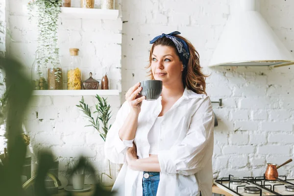 매력적 파란색 청바지와 셔츠를 여성의 사이즈 주방에서 커피를 마시는 — 스톡 사진