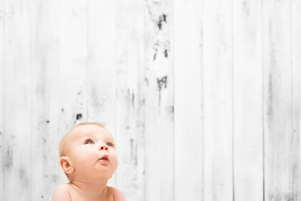 Bebê olhando para cima no fundo de madeira branco — Fotografia de Stock