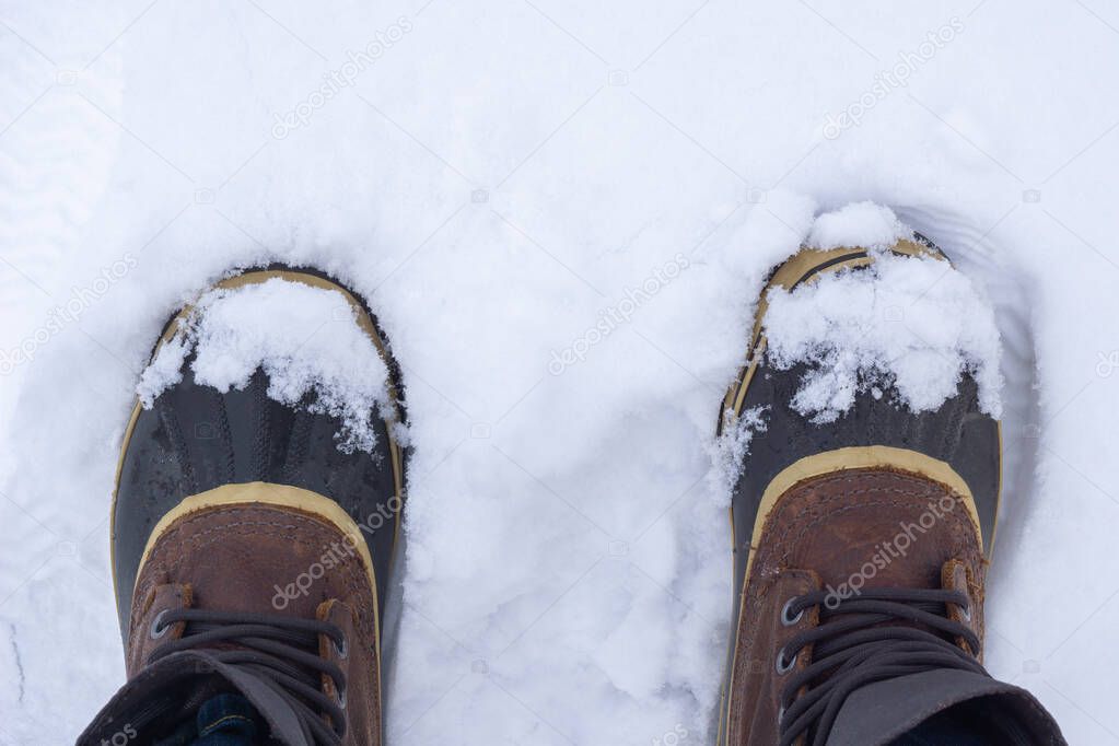 Top view of anonymous traveler in warm boots standing on white snow on winter day.