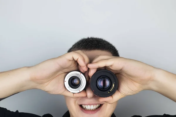 A man tries on two camera lenses instead of eyes. He plays around and fools around. The concept of the photographer\'s work and the creative approach to photography