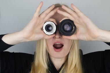 Bir kadın göz yerine iki kamera lensi dener. Oynuyor, oynaşıyor. Fotoğrafçının işi ve fotoğrafçılığa yaratıcı yaklaşım.