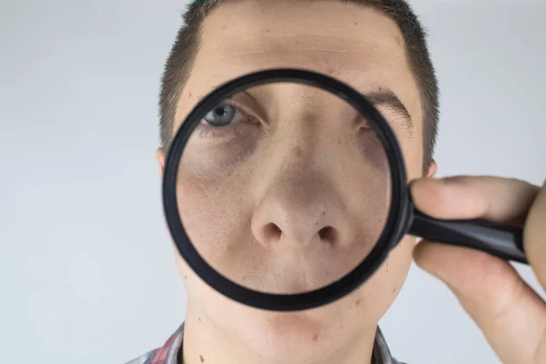 Acne close-up. A man is being examined by a doctor. Dermatologist examines the skin through a magnifier, a magnifying glass