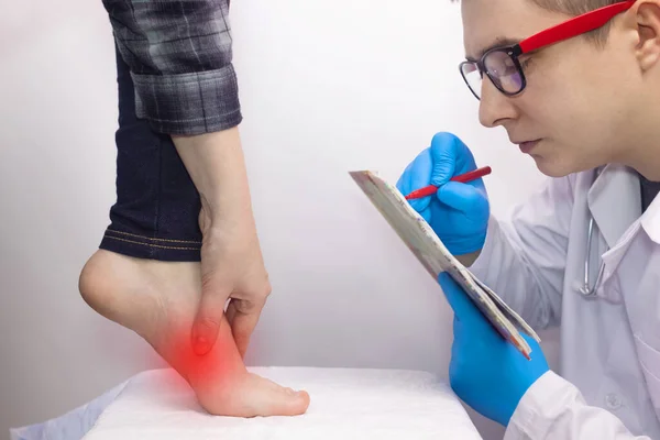 An orthopedic surgeon examines a woman\'s leg. Foot pain, tendon sprains, inflammation, flat feet, bursitis, fasciitis. Foot disease treatment concept. The doctor examines