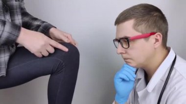Bir kadın diz ağrısından muzdarip. Bir ortopedist ve travmatolog tarafından muayene. Bacağında kızarıklık ve şişkinlik, menisküs yırtılması veya diz kesesi iltihabı. Doktor muayene ediyor.