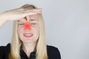 Genç bir kadın burnuna dokunur, ki bu çok acı vericidir. Solunum güçlüğü, tıkanmış burun yolları ve grip, soğuk algınlığı veya koronavirüs için tıbbi bakım konsepti. Bir doktorun muayenesinde..