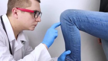 Bir kadın diz ağrısından muzdarip. Bir ortopedist ve travmatolog tarafından muayene. Bacağında kızarıklık ve şişkinlik, menisküs yırtılması veya diz kesesi iltihabı. Doktor muayene ediyor.