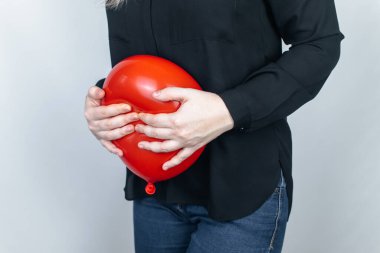 Şişkinlik ve gaz konsepti. Kadın karnının yanında şişkinliği sembolize eden kırmızı bir balon tutuyor. Bağırsak yolu ve sindirim sistemi. Osurma ve gastrointestinal sistemde sorun var. 
