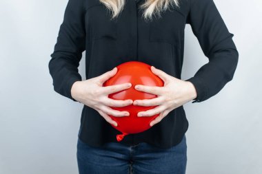 Şişkinlik ve gaz konsepti. Kadın karnının yanında şişkinliği sembolize eden kırmızı bir balon tutuyor. Bağırsak yolu ve sindirim sistemi. Osurma ve gastrointestinal sistemde sorun var. 