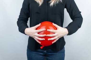 Bloating and flatulence concept. The woman holds a red balloon near the abdomen, which symbolizes bloating. Intestinal tract and digestive system. Problems with flatulence and gastrointestinal tract  clipart