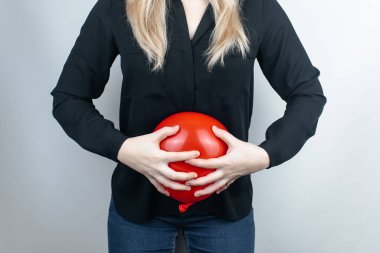 Şişkinlik ve gaz konsepti. Kadın karnının yanında şişkinliği sembolize eden kırmızı bir balon tutuyor. Bağırsak yolu ve sindirim sistemi. Osurma ve gastrointestinal sistemde sorun var. 