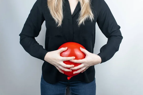 Bloating and flatulence concept. The woman holds a red balloon near the abdomen, which symbolizes bloating. Intestinal tract and digestive system. Problems with flatulence and gastrointestinal tract