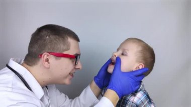 Bir çocuk doktoru boğaz ağrısından şikayet eden bir çocuğu muayene eder. Trakeal hastalıkların teşhisi. Anjin, bademcik iltihabı, gırtlak iltihabı, nazofarinkste ağrı. Çocuk tıbbi bakım konsepti