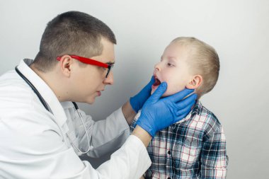 Bir çocuk doktoru boğaz ağrısından şikayet eden bir çocuğu muayene eder. Trakeal hastalıkların teşhisi. Anjin, bademcik iltihabı, gırtlak iltihabı, nazofarinkste ağrı. Çocuk tıbbi bakım konsepti