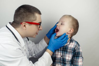 Bir çocuk doktoru boğaz ağrısından şikayet eden bir çocuğu muayene eder. Trakeal hastalıkların teşhisi. Anjin, bademcik iltihabı, gırtlak iltihabı, nazofarinkste ağrı. Çocuk tıbbi bakım konsepti