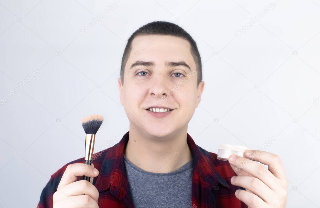 The man looks into the frame and uses powder. Close-up of a guy putting makeup on his face. LGBT community, gay or self-care concept.