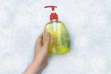 Köpükte bir şişe deterjan yüzüyor. Evdeki kimyasalların tehlikeleri kavramı. Köpükteki sodyum ödüllü maddeler, parabenler, sülfatlar ve diğer kimyasal bileşikler. Sarı kavanozda sıvı sabun.