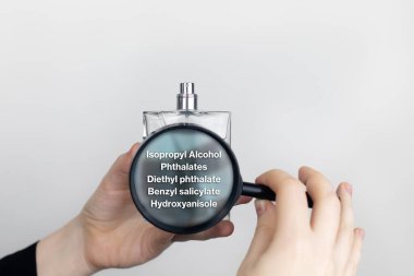Bir kadın parfümün zararlı bileşenlerini büyüteçle inceler. İzopropil alkol, ftalat, dietil ftalat, benzil salisilat, hidroksanisol....