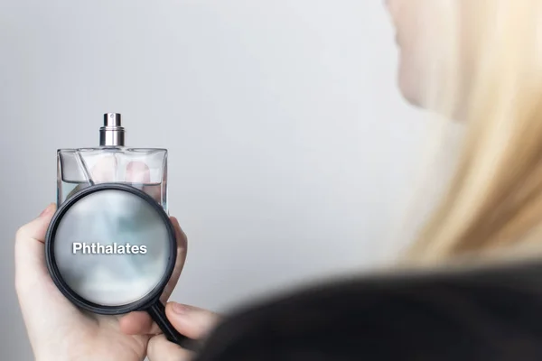 一个女人通过放大镜检查香水的有害成分 用邻苯二甲酸盐化妆品和家用化学品中危险物质的概念 — 图库照片