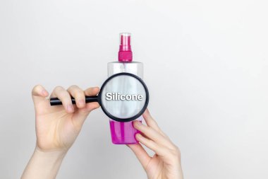 A woman examines the harmful ingredients of the hair spray a magnifying glass. Means with Silicone. The concept of hazardous substances in cosmetics and household chemicals clipart