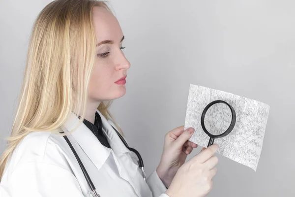 A neurologist with a magnifying glass examines an encephalogram of a patients brain. Schedule of electroencephalograms study of brain currents for signs of epilepsy and pathologies