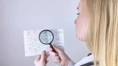 Elinde büyüteç olan bir nörolog hasta beyninin ensefalogramını inceliyor. Epilepsi ve patoloji belirtileri için beyin akımlarını inceleyen elektroensefalogramların programı.