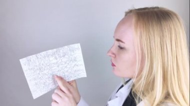 Bir nörolog hasta beyninin ensefalogramını inceler. Epilepsi belirtileri ve sinir sisteminin patolojileri için beyin akımlarını inceleyen elektroensefalogramların programı.